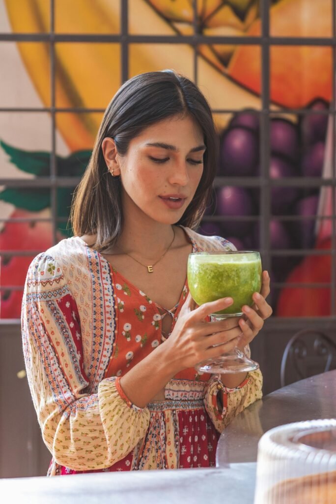 Young woman sipping a healthy green juice indoors, surrounded by vibrant decor.